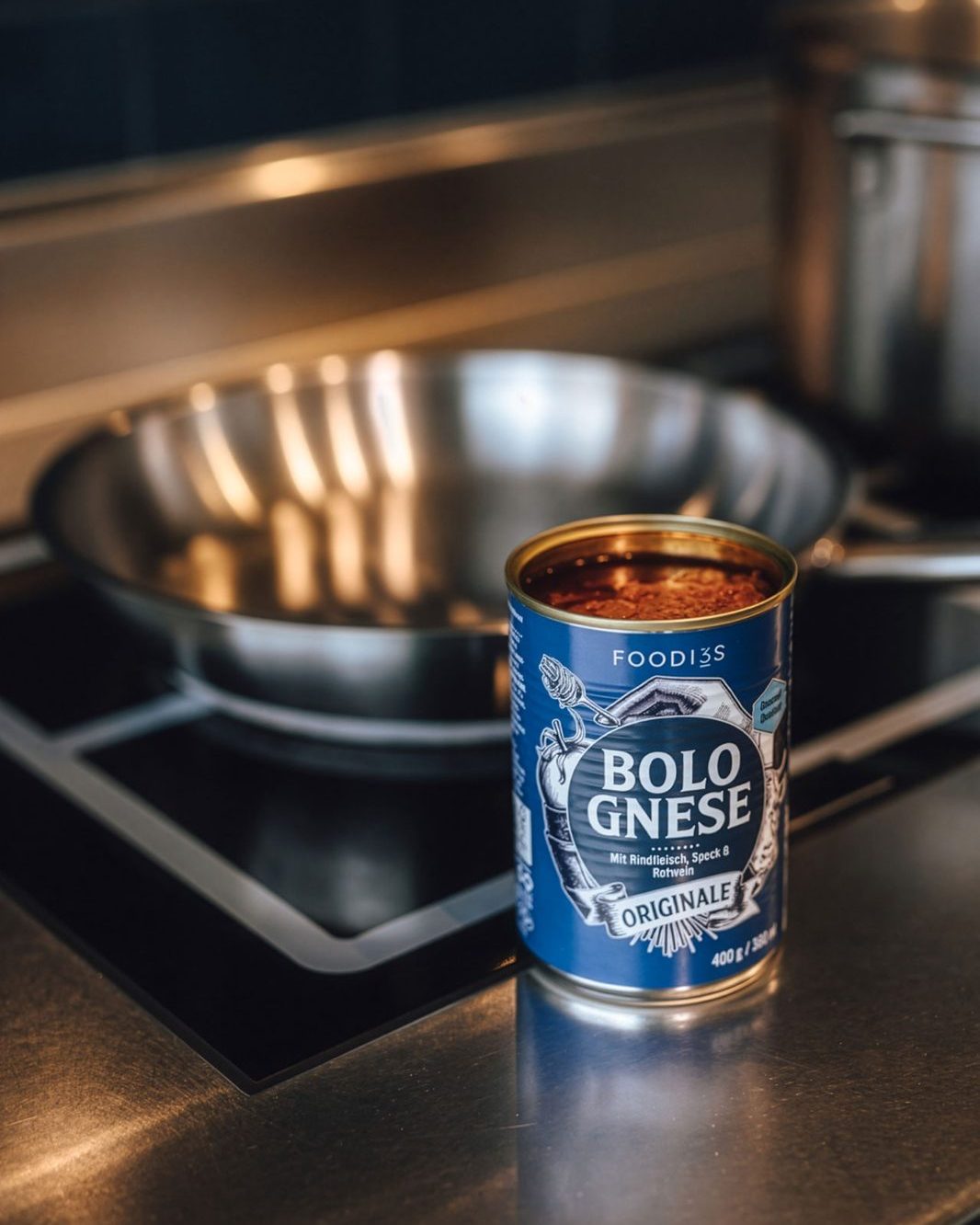 Eine geöffnete Dose 3foodies Bolognese Originale steht auf der Arbeitsplatte vor einer Pfanne auf dem Herd