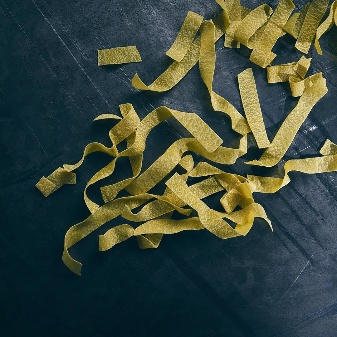 Rohe Pappardelle all’ Uovo auf dunklem Stein – man sieht die raue Oberfläche der Bänder